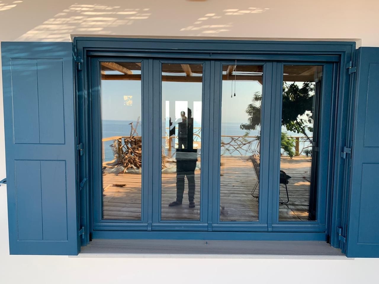 Blue-shuttered doors reflecting the deck and the sea in the glass