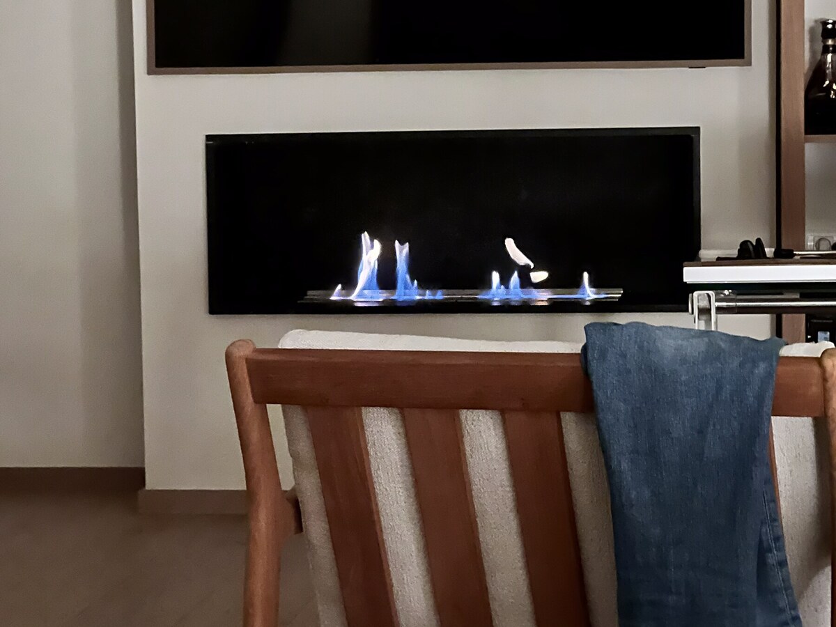 Bio-ethanol fireplace lit in the master suite, blue flames under the wall-mounted TV